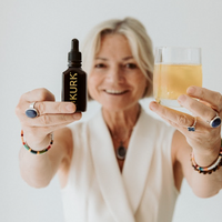 Woman holding a bottle and a glass with 'KURK' branding against a plain background