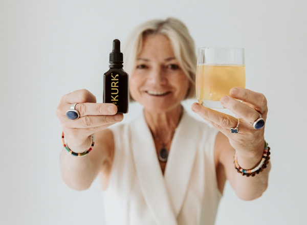 Woman holding a bottle and a glass with 'KURK' branding against a plain background